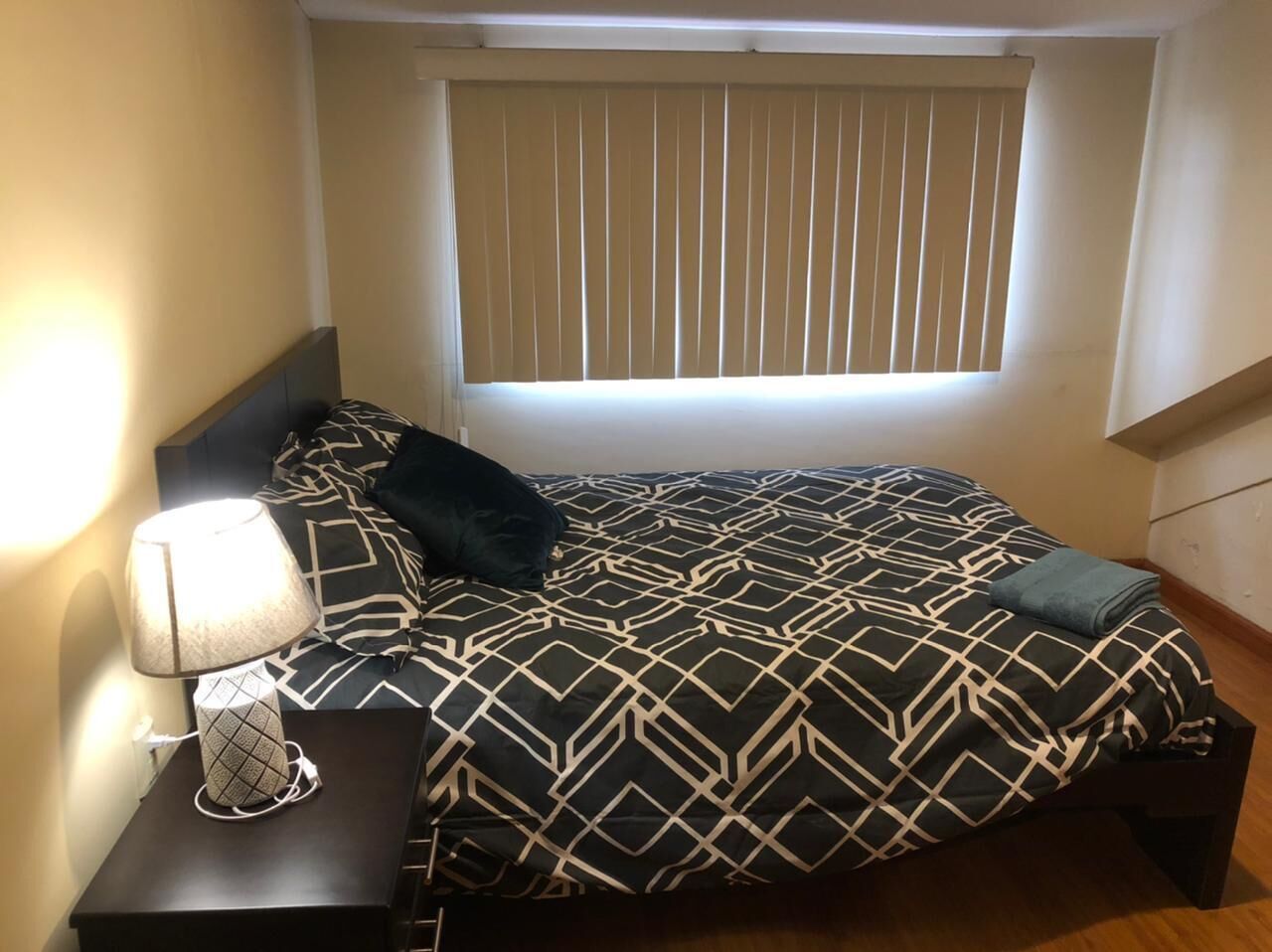 A bedroom with a bed, a nightstand, a lamp, and a window with blinds.