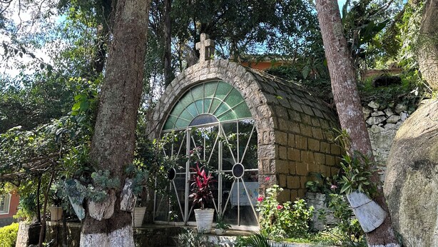 A stone archway with a green glass window, surrounded by trees and plants. - Beautiful Mairiporã Farm with Beach Tennis Court (Mairiporã)