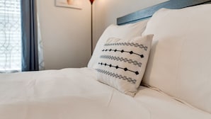 Ein Bett mit weißer Bettwäsche und einem dekorativen Kissen mit geometrischem Muster.