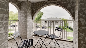Ein Balkon mit rundem Tisch und zwei Stühlen, umgeben von verwitterten Mauern und einem Metallgeländer.