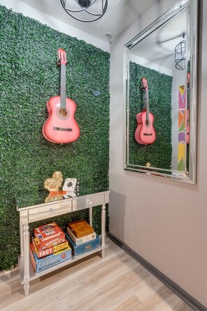 Una habitación con una pared verde, una guitarra rosa, un espejo y una mesita con cajas.
