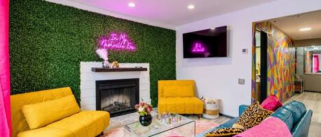 Un salon moderne avec une cheminée, deux canapés jaunes, une table basse en verre et un mur d’un vert éclatant.