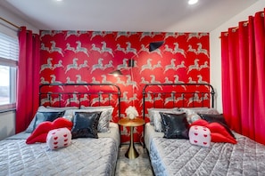 Una habitación con dos camas, cortinas rojas, un papel tapiz con estampado de cebra y una pequeña mesa redonda con una lámpara.