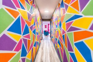 A hallway with colorful geometric patterns on the walls, a wooden floor, and a blue chair in the distance. - Comfortable Chic condo near Riverfront with views (Nashville)
