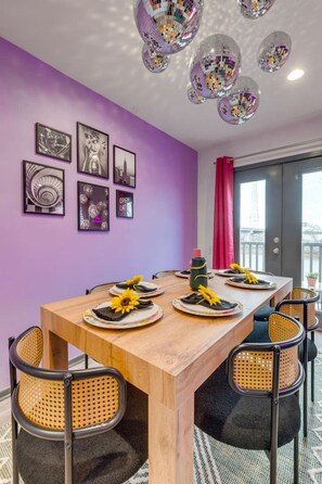Ein Essbereich mit einem Holztisch, Stühlen und einer violetten Wand mit gerahmten Bildern.