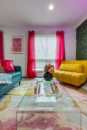 A living room with a glass coffee table, two sofas, a decorative vase, and a window with curtains.