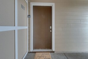 Una puerta con una placa de número, un felpudo y una pared con un diseño de panel.