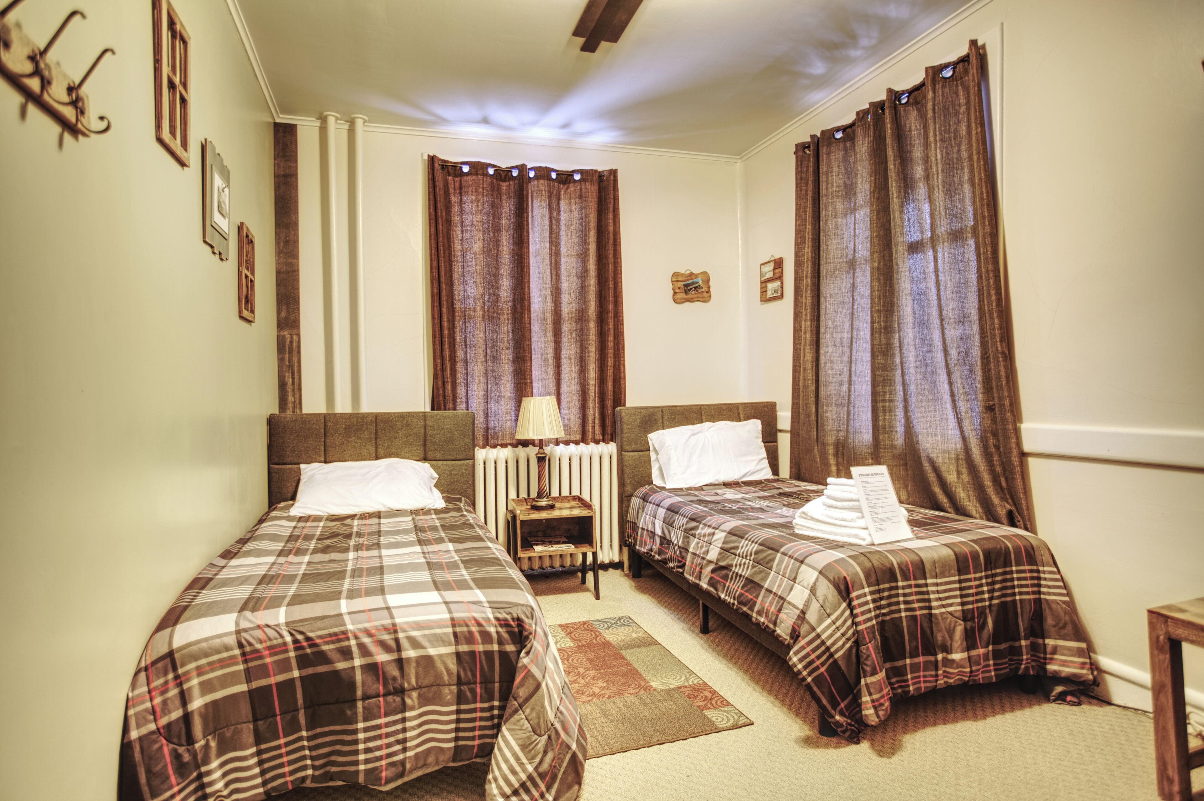 A hotel room with two beds, a nightstand, a lamp, and a radiator.