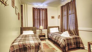 A hotel room with two beds, a nightstand, a lamp, and a radiator.