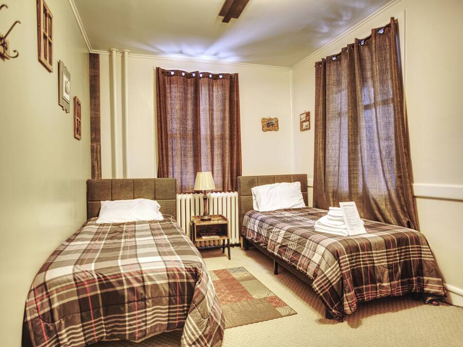 A hotel room with two beds, a nightstand, a lamp, and a radiator.