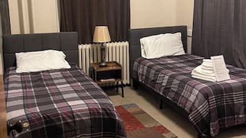 Une chambre d’hôtel avec deux lits, une table de chevet avec une lampe, un radiateur et une petite étagère.
