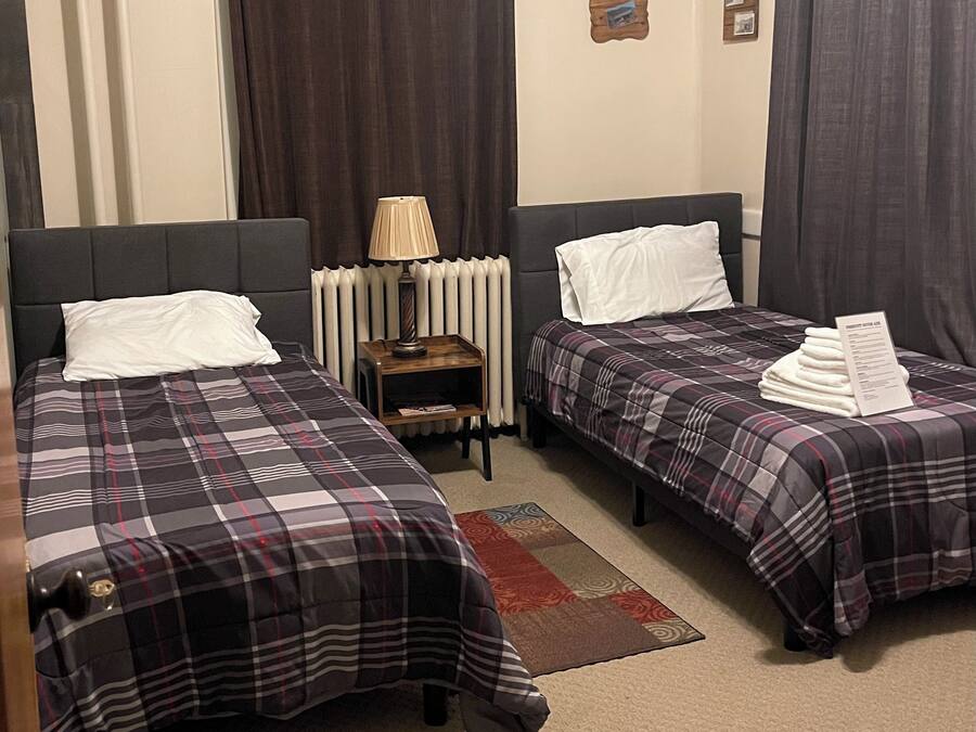 Une chambre d’hôtel avec deux lits, une table de chevet avec une lampe, un radiateur et une petite étagère.