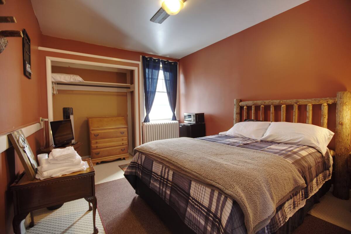 A bedroom with a bed, a dresser, a mirror, a radiator, and a window with curtains.