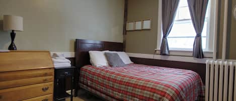 A bedroom with a bed, dresser, lamp, window, and radiator.