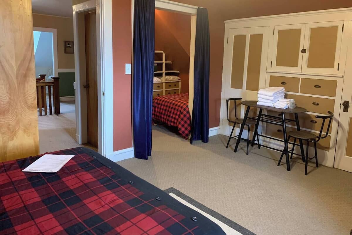 A hotel room with a bed, a desk with chairs, a table with towels, and a wardrobe.