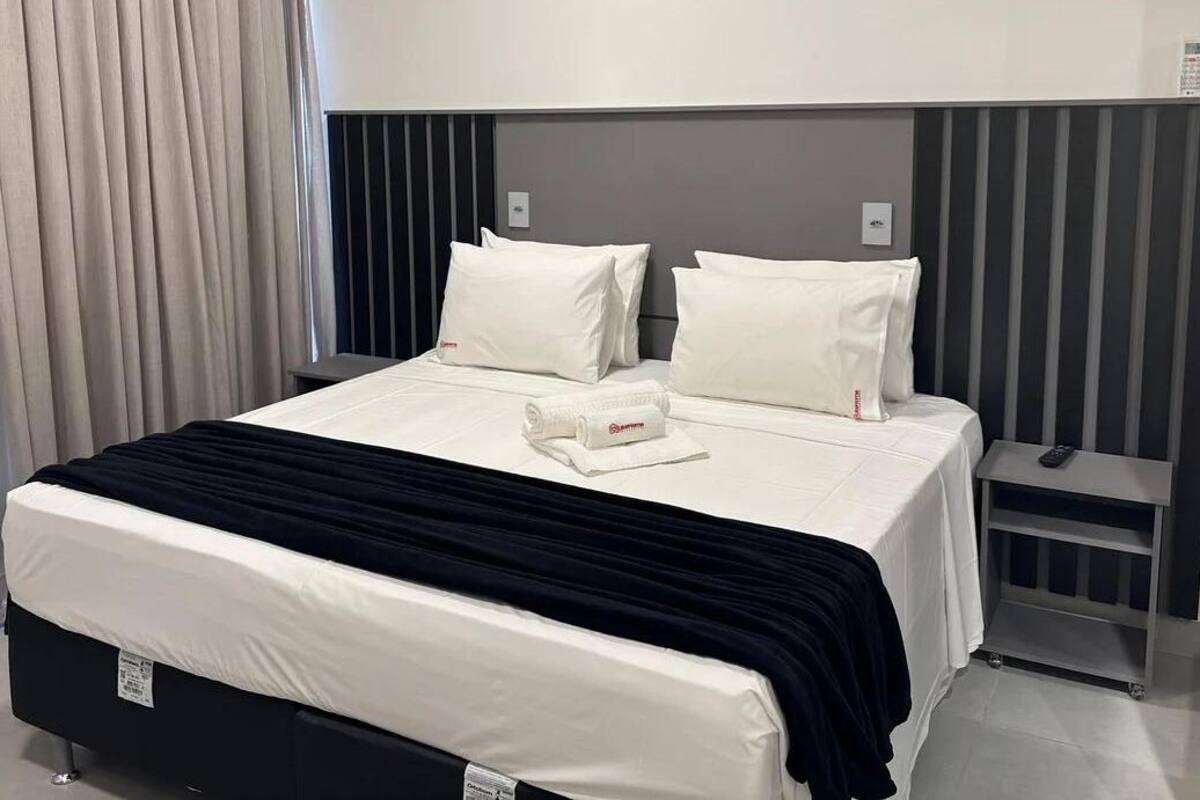 A hotel room with a bed, a nightstand, and a control panel on the wall.