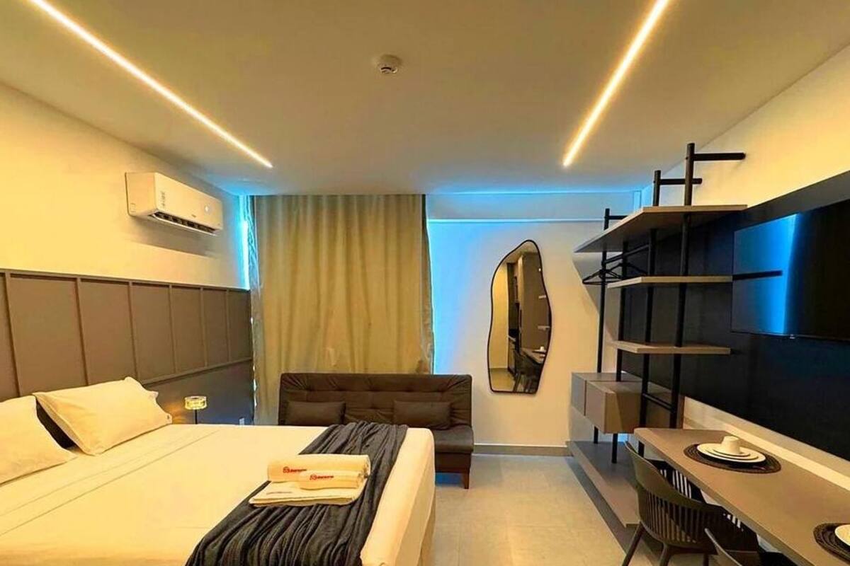 A modern hotel room with a bed, a sofa, a desk, and a TV.