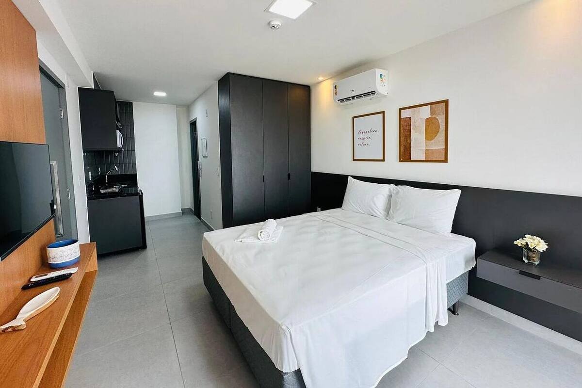 A modern hotel room with a bed, a desk, a TV, and a kitchenette.
