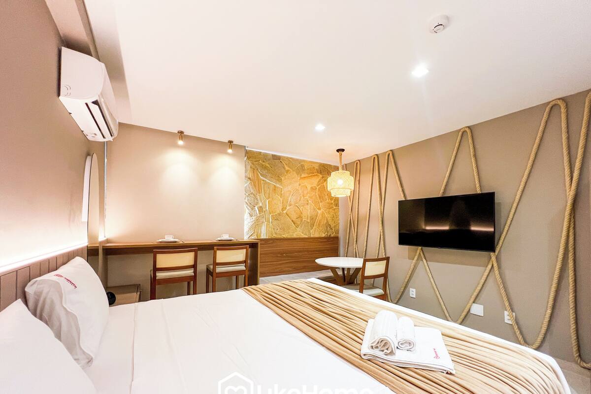 A hotel room with a bed, a desk, chairs, a TV, and a stone wall.