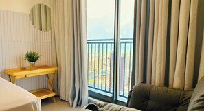 A room with a balcony, a wooden side table, a grey sofa, and a view of buildings. - Simple Smart - LikeHome Hospedagens (João Pessoa)