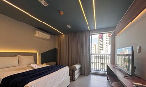 Ett modernt hotellrum med en säng, ett skrivbord, en TV och en balkong med utsikt över staden.