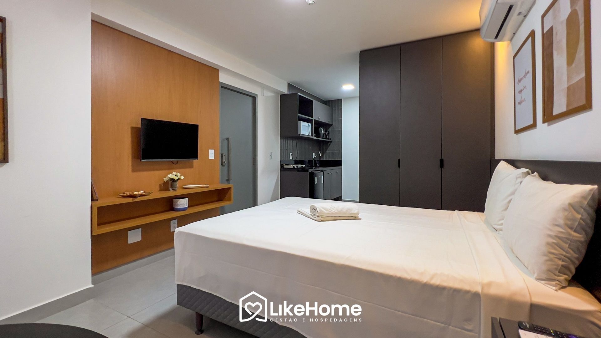 Quarto de hotel com cama, televisão, pequeno espaço de cozinha e guarda-roupa.