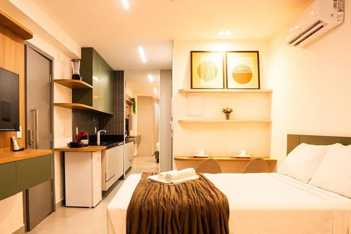 A modern hotel room with a bed, a TV, a kitchenette, and a small bathroom.