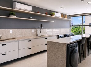 A modern kitchen with a large island, built-in appliances, and a window with a city view. - Simple Smart - LikeHome Hospedagens (João Pessoa)