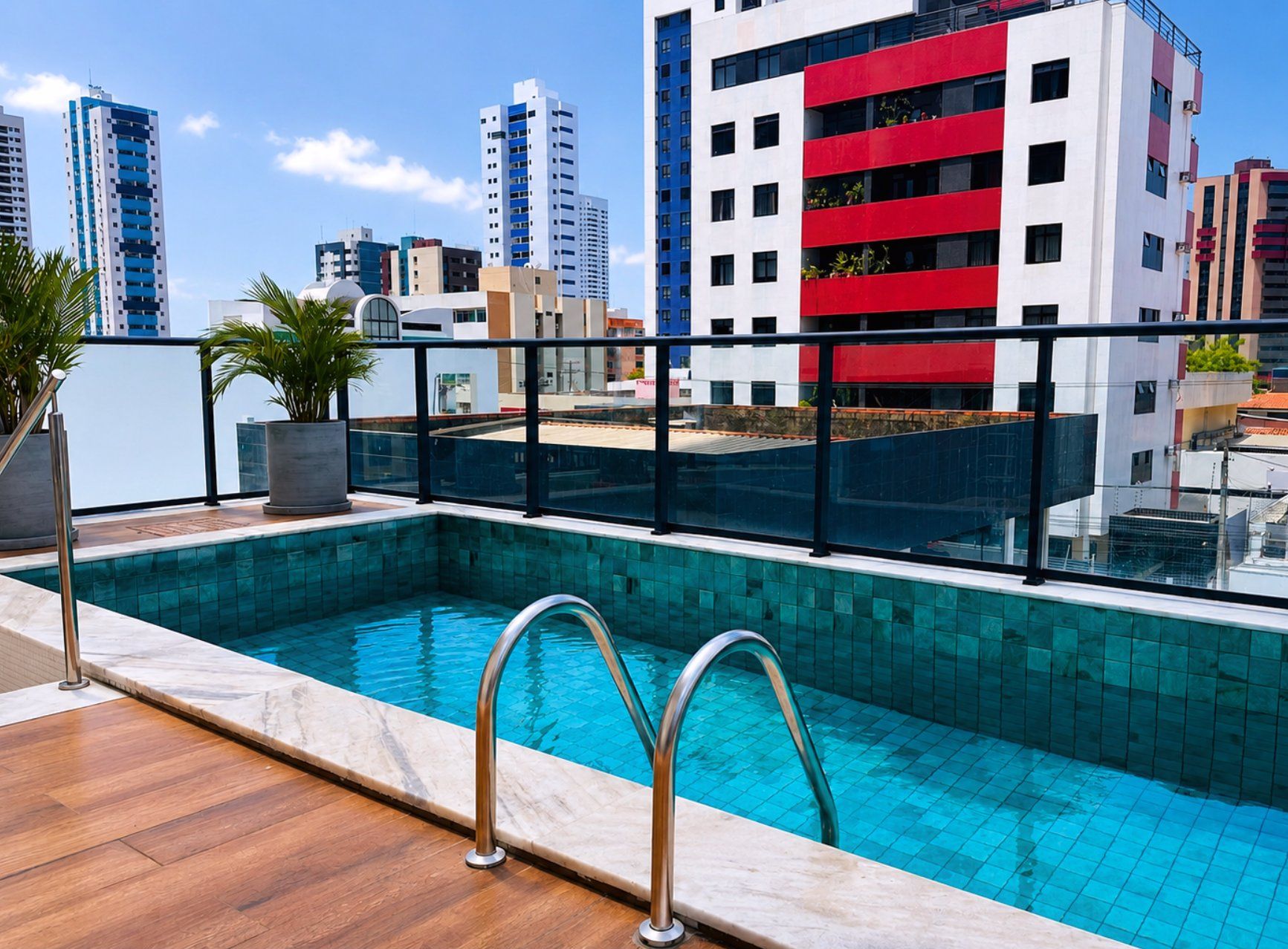 Una piscina sul tetto con ringhiera in vetro, circondata da edifici moderni.