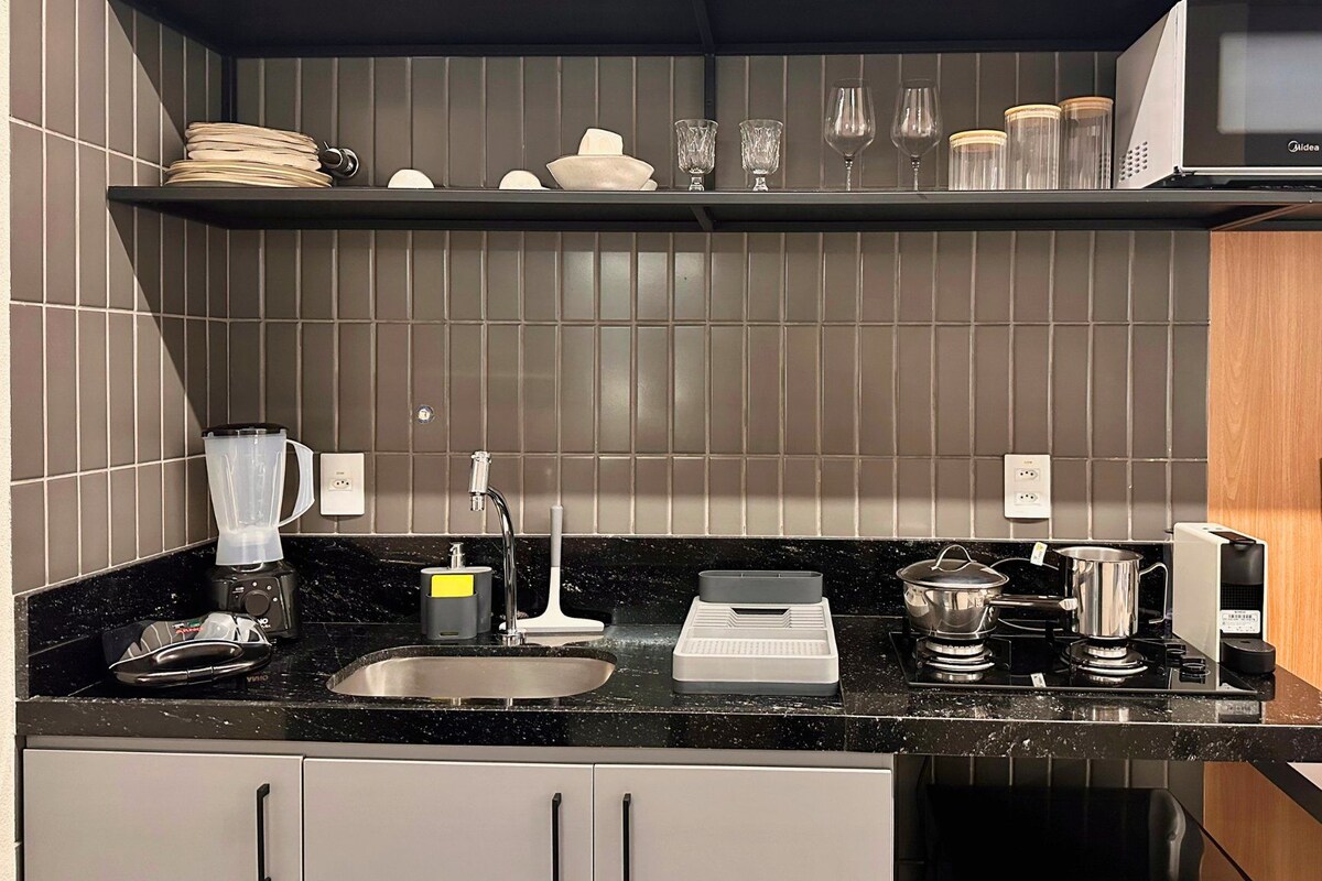 A modern kitchen with a black countertop, stainless steel sink, and a microwave above the counter.