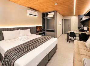 Una habitación de hotel con cama, mesita de noche, armario y una pequeña cocina.