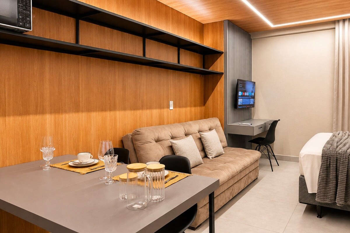 A modern hotel room with a sofa, a desk, a television, and a dining area with table and chairs.