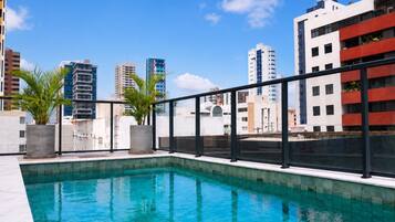 Una piscina en la azotea con vistas a la ciudad, rodeada de edificios y plantas en macetas.