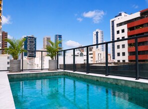 A rooftop pool with a cityscape view, surrounded by buildings, and potted plants. - Simple Smart - LikeHome Hospedagens (João Pessoa)