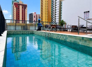 Una piscina al aire libre con borde de azulejos, rodeada de sillas de descanso y una escalera.