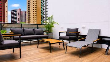 A rooftop lounge with a sofa, chairs, a small table, and a potted plant.