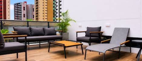 A rooftop lounge with a sofa, chairs, a small table, and a potted plant.