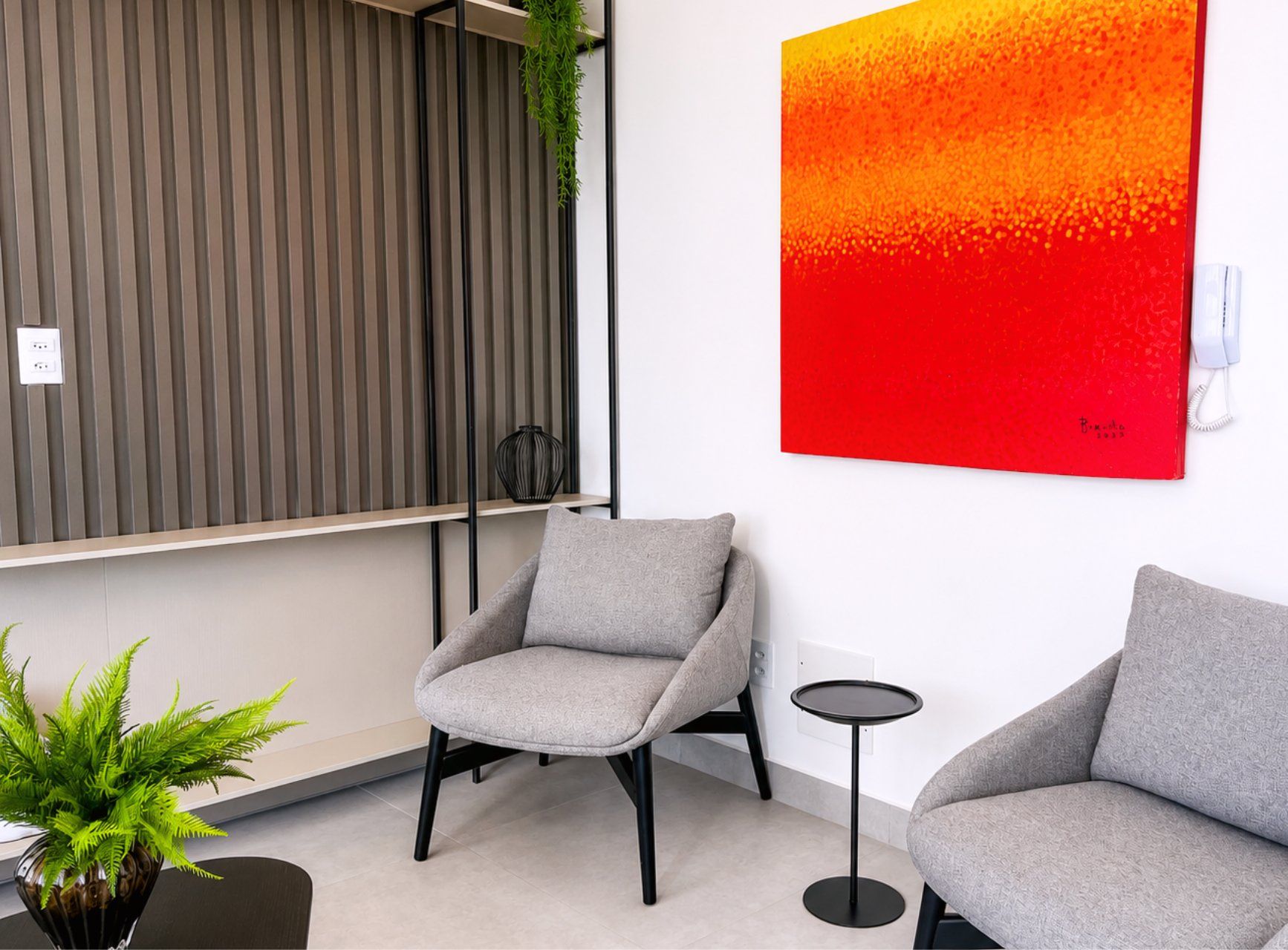 A modern interior with two grey armchairs, a small round table, a potted plant, and a red abstract painting on the wall.