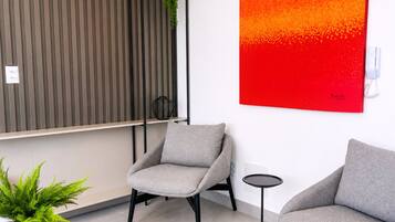 Un interior moderno con dos sillones grises, una mesita redonda, una planta en maceta y un cuadro abstracto rojo en la pared.