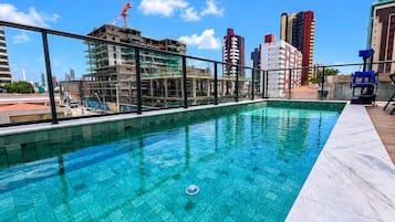 Une piscine sur le toit offrant une vue sur le paysage urbain, notamment sur un chantier de construction et des immeubles de grande hauteur.