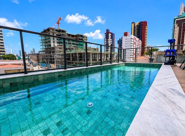 Una piscina en la azotea con vistas a un paisaje urbano, incluyendo una obra en construcción y edificios altos.