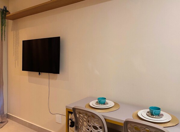 A room with a flat-screen TV mounted on the wall, a dining table with two chairs, and a small plant on the left. - Simple Smart - LikeHome Hospedagens (João Pessoa)
