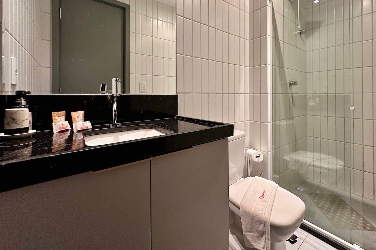 Ein Badezimmer mit schwarzem Waschtisch, einem Waschbecken, einem Spiegel und einer gläsernen Duschkabine.