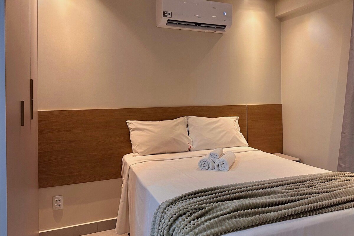 Habitación de hotel con cama, cabecera, equipo de aire acondicionado y una toalla sobre la cama.