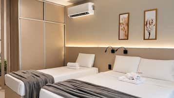 A hotel room with two beds, a wall-mounted air conditioner, and two framed artworks.