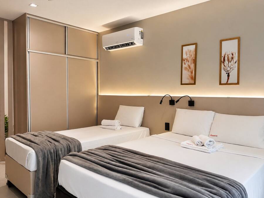 Une chambre d’hôtel avec deux lits, un climatiseur fixé au mur et deux œuvres d’art encadrées.