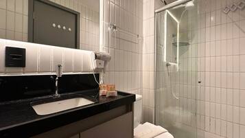 Un baño moderno con encimera negra, lavabo blanco, secador de pelo y cabina de ducha de vidrio.