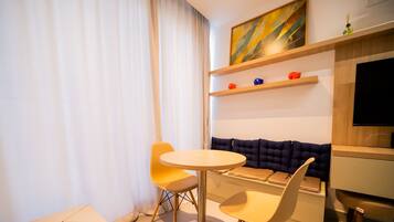 Habitación de hotel moderna con una mesa redonda, un sofá y un ventanal con cortinas.