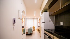 Ett kompakt hotellrum med ett litet pentry, en säng med ett blått överkast, en liten sittgrupp och en spegel.