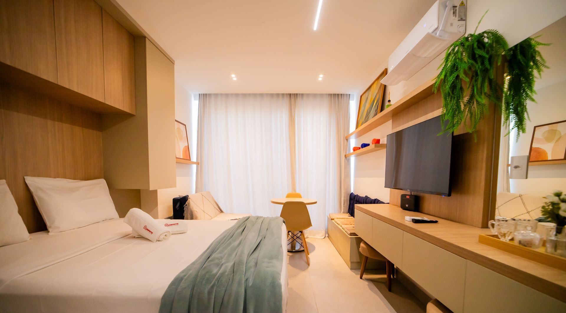 A hotel room with a bed, bedside table, TV, and a desk with a chair.